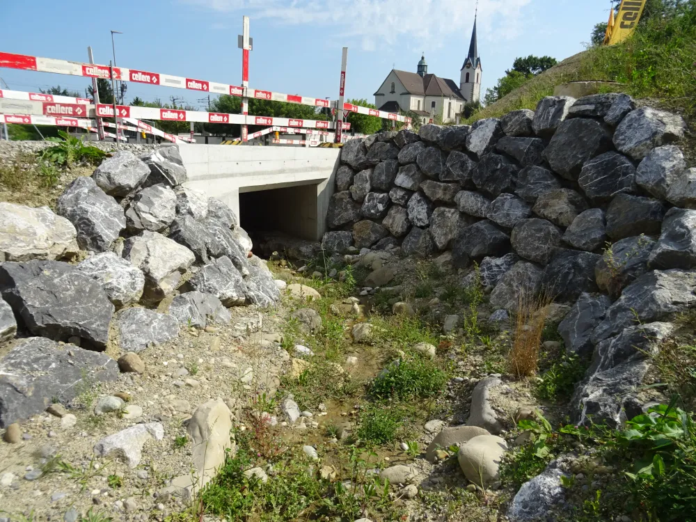 Mauer aus grossen Steinen neben einer Betonunterführung für den Bach