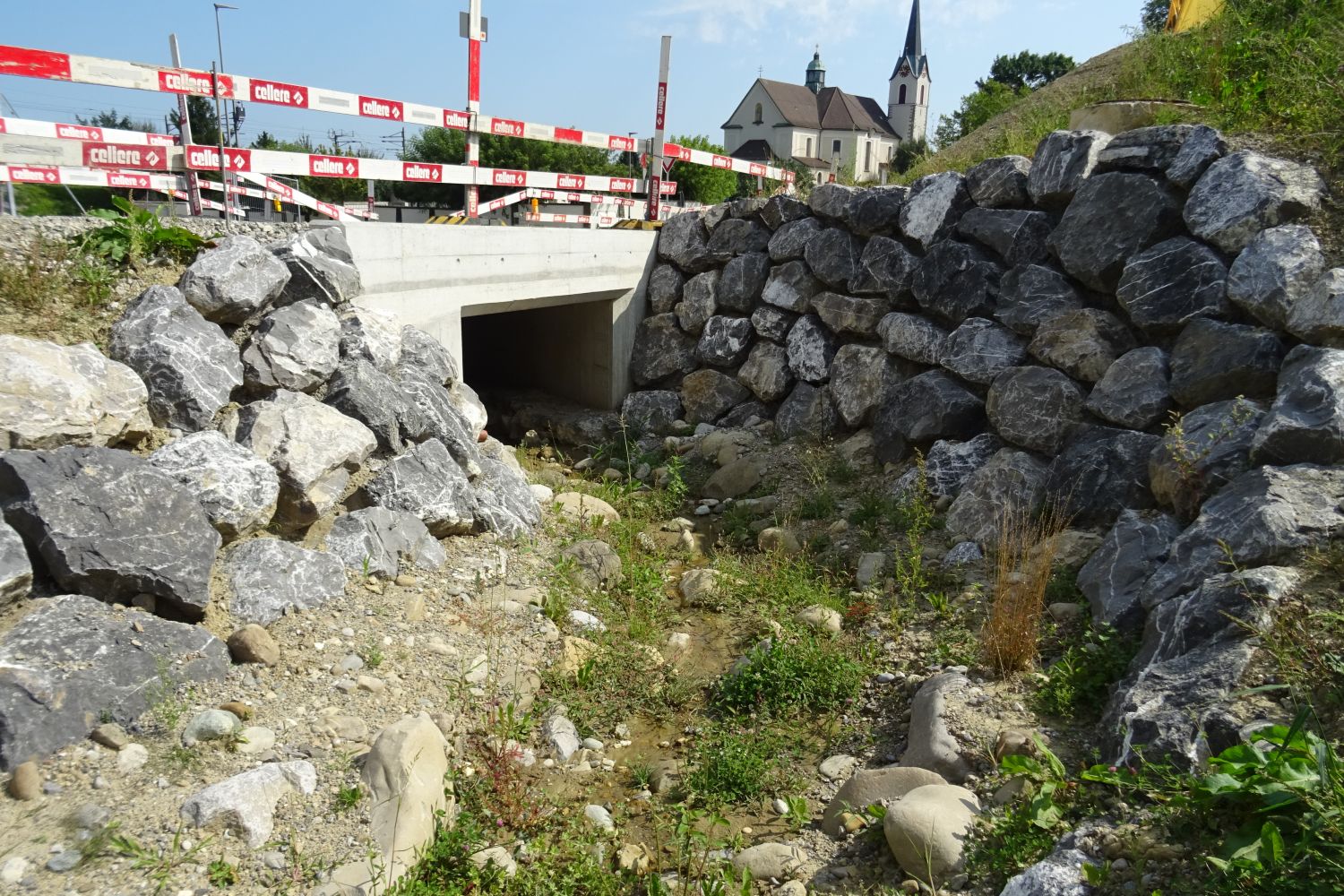 Mauer aus grossen Steinen neben einer Betonunterführung für den Bach