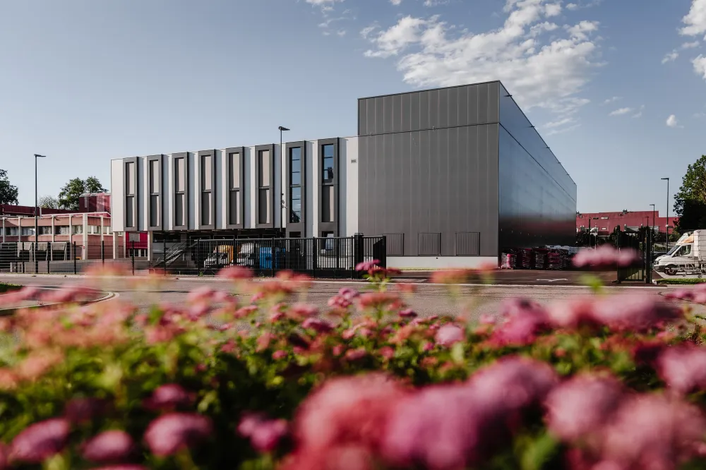 Durch ein Blumenbeet sieht man das neugebaute Gebäude bei gutem Wetter. 